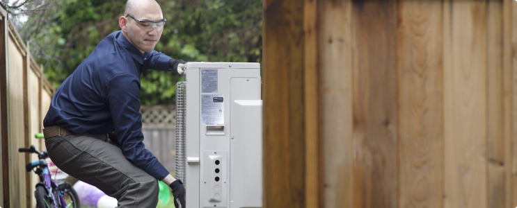 An HVAC technician wearing protective glasses is installing a heat pump unit.