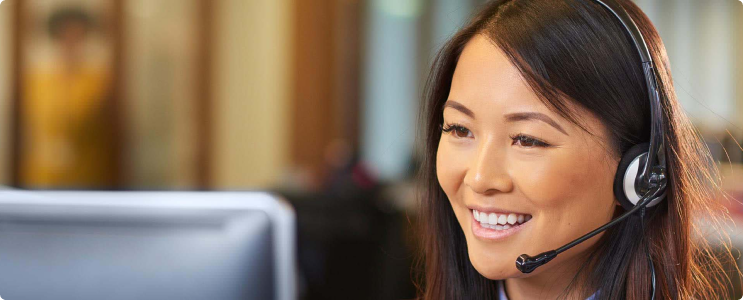 An Asian woman is working as a customer service representative. She is wearing a headset with a desktop computer in front of her.