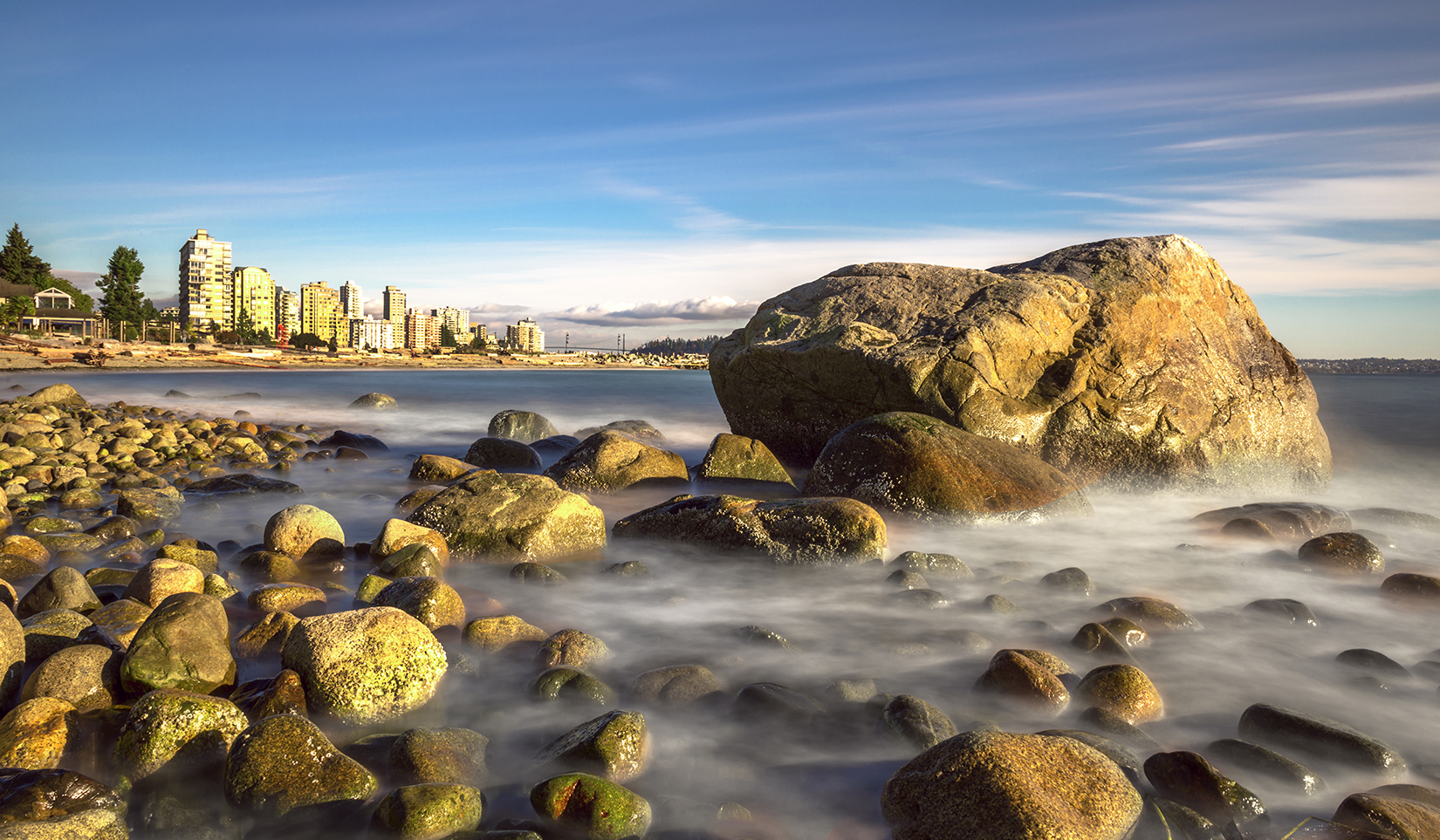 A view of a rocky beach. In the background sits West Vancouver.